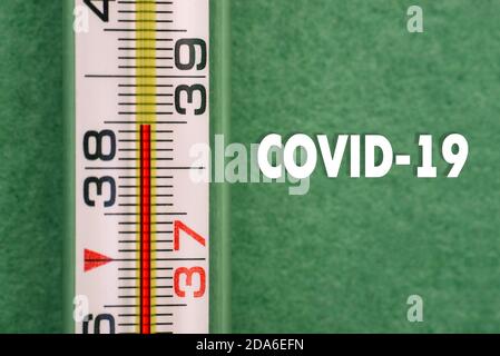 Primo piano del termometro ad alta temperatura con il testo COVID-19. Segni della malattia del coronavirus. Sintomi virali. Controlli della temperatura corporea Foto Stock