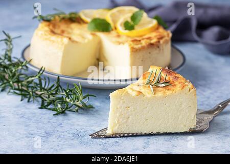 Cheesecake alla vaniglia al limone decorato con rosmarino, menta e fette di limone. Ricotta senza cheesecake alla crosta o casseruola. Sfondo blu. Foto Stock