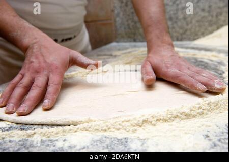 il pizzaiolo spalma con la sua pasta di pane lievitato mani prima di mettere la pizza nel forno Foto Stock