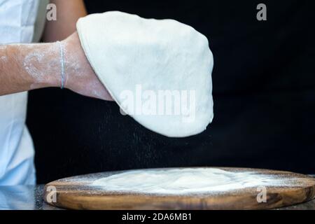 Dettaglio delle mani di uno chef pizzeria che lavora per le varie fasi di preparazione di una vera pizza italiana fatta in casa con farina di lievito e acqua. Foto Stock