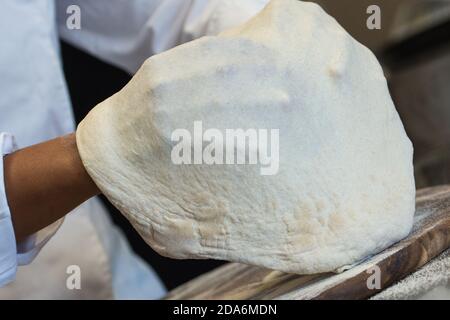 Dettaglio delle mani di uno chef pizzeria che lavora per le varie fasi di preparazione di una vera pizza italiana fatta in casa con farina di lievito e acqua. Foto Stock