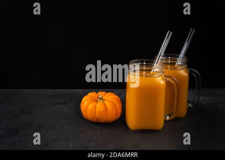 Zucca intera, vasetti di vetro quadrati con coda di mocktail non alcolica e cannucce di vetro su superficie nera. Sfondo orizzontale per Halloween con copia Foto Stock
