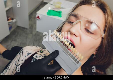 Primo piano ritratto di giovani donne in sedia dentista, controllare e selezionare il colore dei denti. Il dentista fa il processo di trattamento nella clinica dentale Foto Stock