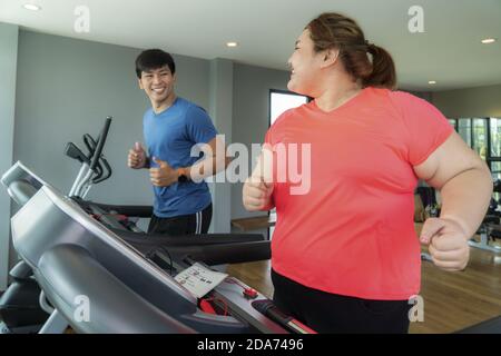 Due Asian trainer uomo e donna sovrappeso esercizio di formazione sul tapis roulant in palestra, trainer thump fino a lei per il buon risultato durante gli allenamenti. Donne grasse Foto Stock