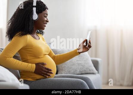 Donna nera incinta che ascolta la musica utilizzando l'app mobile Foto Stock