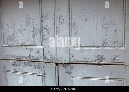 una vista ravvicinata di una vecchia doppia dipinta di bianco porta in cui la vernice si stacca per mostrare il rivestimento inferiore Foto Stock