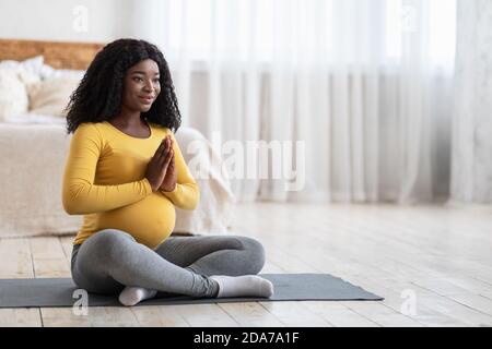 Donna serena incinta nera meditando a casa Foto Stock