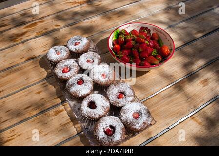 Fragole rosse mature in ciotola e cupcake appena sfornati su tavola di legno all'aperto. Vista ad angolo alto. Foto Stock