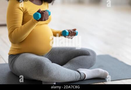 Donna incinta irriconoscibile che si esercita con manubri a casa Foto Stock