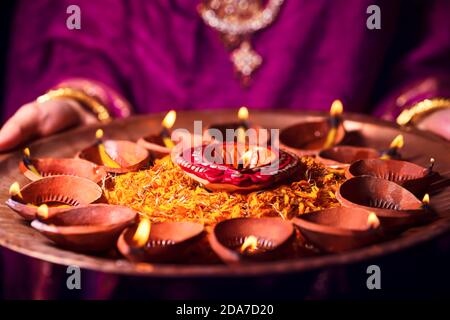 Felice Diwali sfondo. Donna indiana o sposa che indossa stoffa tradizionale e gioielli, tenendo puja thali pieno di luce bruciante diya o lampade ad olio di argilla, d Foto Stock