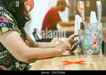 Donna che usa telefoni cellulari per lavorare con immagine sfocata di il contrassegno di posto alternativo per la distanza sociale regola la distanza per uno sedile da altre persone a. Foto Stock