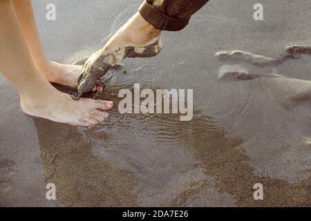 I piedi dell'uomo toccano i piedi di una donna con vernice rosa per unghie, su una spiaggia di Bali Foto Stock