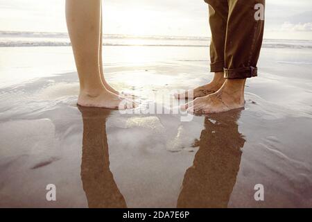 Piedi dell'uomo davanti ai piedi di una donna con vernice rosa per unghie, su una spiaggia di Bali Foto Stock