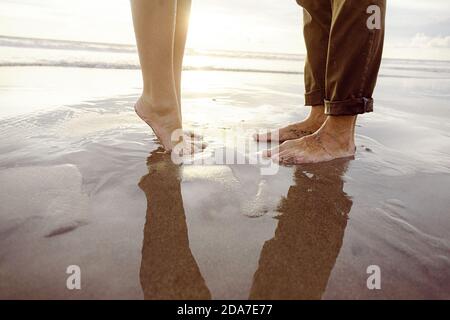 I piedi dell'uomo davanti ai piedi di una donna, sollevando, con vernice rosa per unghie, su una spiaggia di Bali Foto Stock