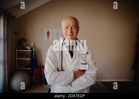 Ritratto di un medico senior di successo che indossa un camice da laboratorio con stetoscopio e. braccia incrociate in piedi guardando la telecamera Foto Stock