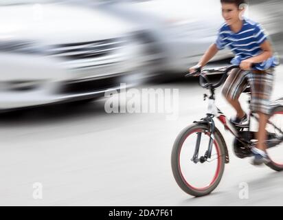 Pericolosa situazione del traffico cittadino con un ragazzo in bicicletta e auto in movimento sfocato. Sfocatura intenzionale del movimento Foto Stock