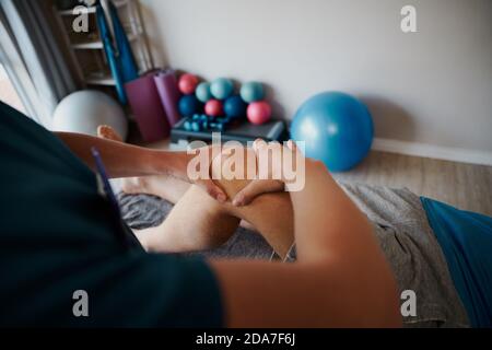 Primo piano di una giovane fisioterapista femminile che aiuta l'uomo con l'esercizio al ginocchio Foto Stock