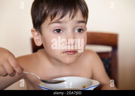 Il ragazzino mangia con un cucchiaio da un piatto Foto Stock