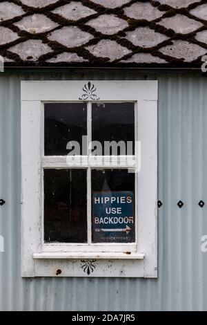 Avviso nella finestra di un edificio in ferro corrugato sulle Highlands occidentali della Scozia, che chiede "Hippies use back door, no exceptions". Foto Stock