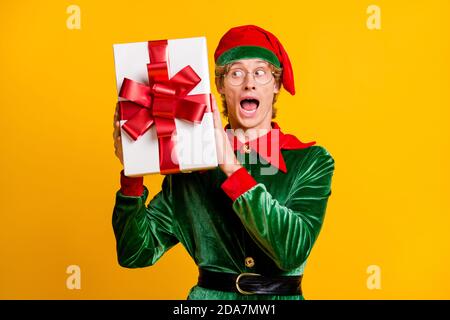 Ritratto del suo bello attraente stupito allegro allegria divertente guy elfo che tiene in mani giftbox indovinare ciò che è dentro avere divertimento isolato Foto Stock