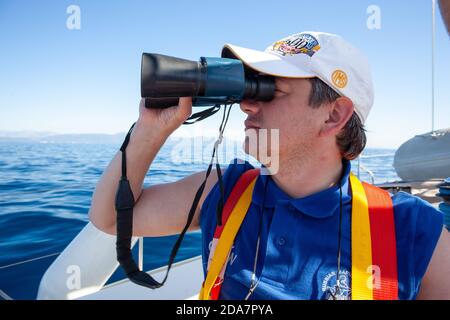 Grecia. Corfù 25 ottobre 2016: Un giovane marinaio maschile su uno yacht a vela guarda attraverso il binocolo Foto Stock