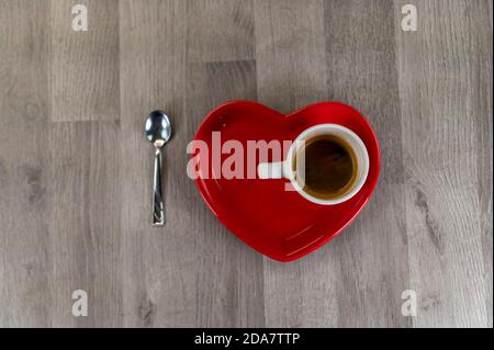 una tazza di caffè con un piatto a forma di cuore e un cucchiaino da tè Foto Stock