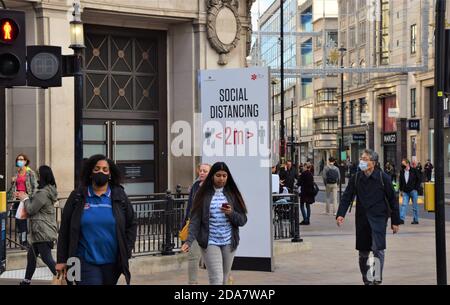 La gente passa accanto a un cartello Social Distancing su Oxford Street, Londra durante il secondo blocco nazionale in Inghilterra. Foto Stock