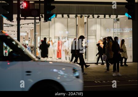 LONDRA - 3 NOVEMBRE 2020: Gli acquirenti di silhouette passano davanti a un grande magazzino ben illuminato su Oxford Street Foto Stock