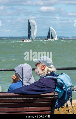 una coppia più anziana o di mezza età seduta al mare guardando gli yacht e le barche durante la regata della settimana di cowes sul isola di wight regno unito Foto Stock