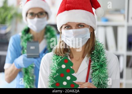 Due dottori in maschere mediche protettive e cappelli babbo natale sorridono. Foto Stock