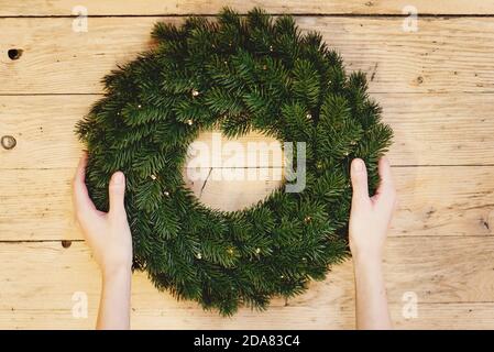 Vista dall'alto delle mani della donna che tengono la corona di Natale su sfondo di legno. Foto Stock