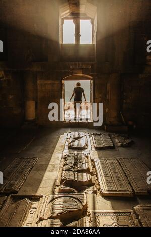 Uomo che segue la luce in un monastero armeno. Giovane maschio sulla strada per la luce. Potenza della luce. Raggio di luce. Misteriosa atmosfera tranquilla Foto Stock