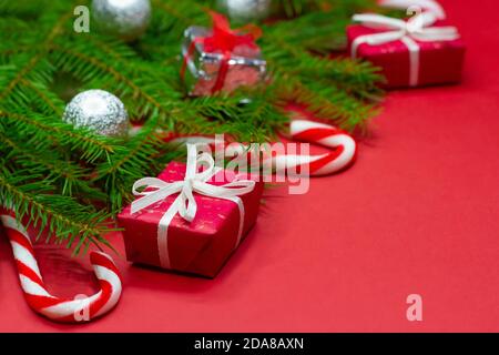 Primo piano di rami di albero di natale decorato con scatole regalo, palle di natale e canne caramelle su sfondo rosso con spazio di copia. Foto Stock