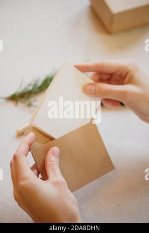 Primo piano di mani femminili che mettono il biglietto d'auguri in una busta di carta artigianale. Foto Stock