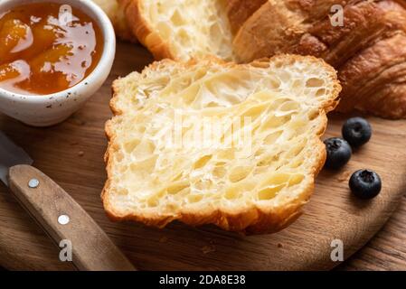 Croissant a metà. Croissant tagliato longitudinalmente su tavola di legno, vista closeup. Pasticceria francese Foto Stock