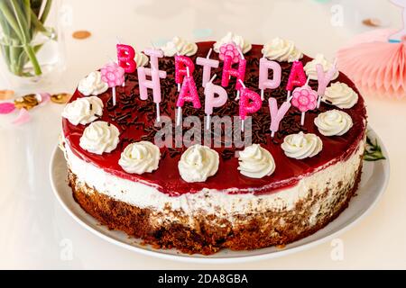 Torta di compleanno fatta in casa con candele di lettera con spruzzette di cioccolato e macchie di crema, sparato direttamente su un tavolo decorato in vetro bianco con confetti do Foto Stock