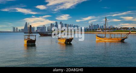 Lo skyline di Doha dalla passeggiata della Corniche è stato girato nel pomeriggio con i dhows Bandiera del Qatar nel golfo arabo in primo piano e nuvole in il cielo sullo sfondo Foto Stock