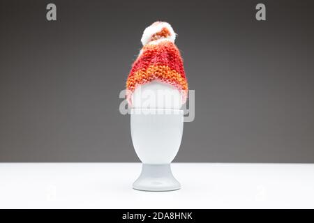 coppa d'uovo con uovo e un cappuccio di lana rosso arancione fatto in casa su sfondo grigio scuro su un tavolo bianco, spazio per la copia di testo o biglietti d'auguri per pasqua o chris Foto Stock