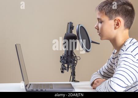 Bambino con computer portatile che parla nel microfono. Tecnologia, apprendimento online, formazione a distanza, apprendimento a distanza a casa Foto Stock