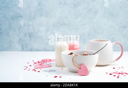 Colazione su sfondo romantico. Cereali in una tazza bianca, caffè con latte e cuori su fondo blu e bianco. Foto Stock