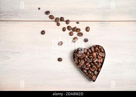 Cuore di caffè su sfondo chiaro. Un cuore volante con una coda di grani sparsi. Foto Stock