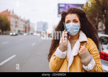 Bella donna afro capelli indossando maschera medica protettiva supporto per strada e per telefono Foto Stock