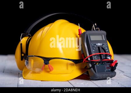 Un casco e occhiali protettivi su un banco da lavoro. Accessori per lavori elettrici in officina. Sfondo scuro. Foto Stock