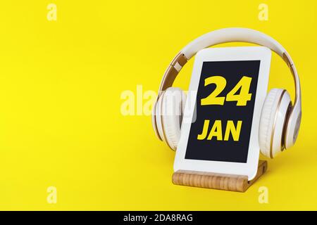 24 gennaio. Giorno 24 del mese, data del calendario. Cuffie eleganti e moderno tablet su sfondo giallo. Spazio per il testo. Istruzione, tecnologia, vita Foto Stock