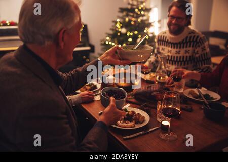 Uomo anziano che passa il cibo a suo figlio sul tavolo da pranzo. La famiglia ha una deliziosa cena di ringraziamento a casa. Foto Stock