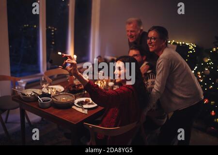 Famiglia che prende selfie al tavolo di Natale. Donna scattando ritratto selfie con la famiglia alla vigilia di Natale a casa. Foto Stock
