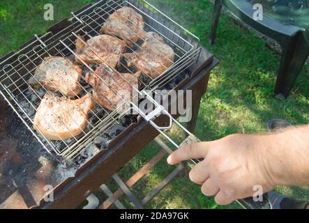 Primo piano di una mano dell'uomo che prepara carne fritta, all'aperto, in estate, sullo sfondo dell'erba Foto Stock