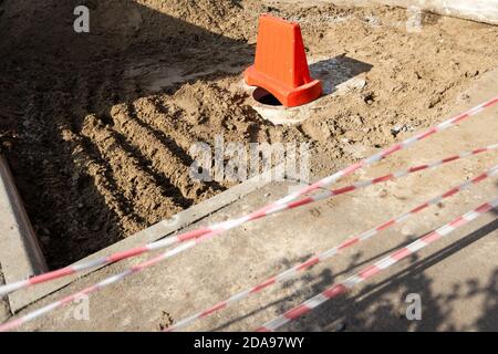 Pericoloso botola aperta senza coperchio e una recinzione di avvertimento sulla strada Foto Stock