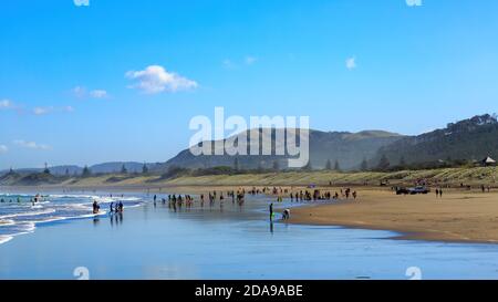 Vista panoramica della spiaggia di sabbia nera a Muriwai , Nuova Zelanda, in una giornata di sole con una folla di turisti Foto Stock