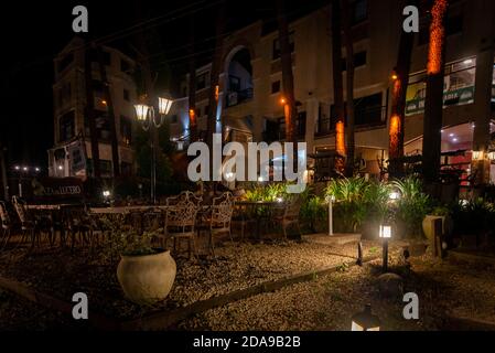 Scena notturna di un elegante bar all'aperto illuminato da piccole lampade tra alberi e piante Foto Stock